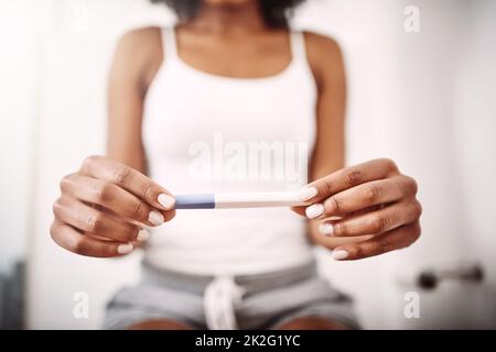 Ist es zu früh, um mit Namen zu beginnen? Aufnahme einer nicht erkennbaren Frau, die einen Schwangerschaftstest hält, während sie auf der Toilette sitzt. Stockfoto