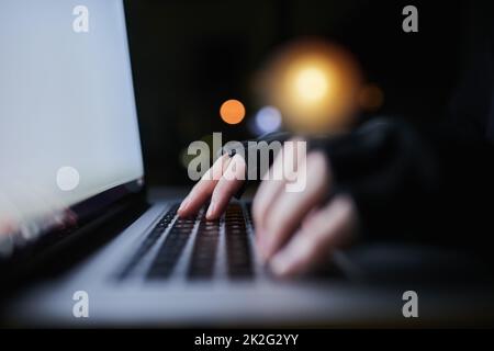 Seien Sie vorsichtig, was Sie online teilen. Aufnahme eines nicht erkennbaren Computerhackers, der spät in der Nacht einen Laptop benutzt. Stockfoto