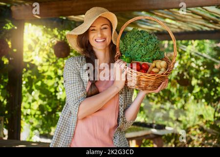 Gesundes Leben beginnt im Garten. Porträt einer jungen Frau, die einen Korb mit frisch gepflückten Produkten in einem Garten trägt. Stockfoto