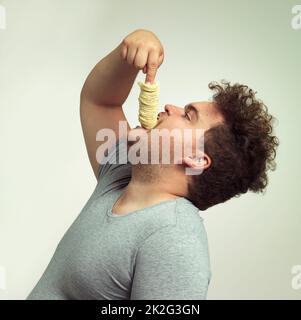 Für meinen nächsten Trick werde ich diese Chips verschwinden lassen. Studioaufnahme eines übergewichtigen Mannes, der einen Stapel Chips in den Hals schiebt. Stockfoto