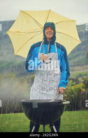 Es ist wie flüssiger Sonnenschein. Aufnahme eines Mannes, der im Regen fröhlich grillt. Stockfoto