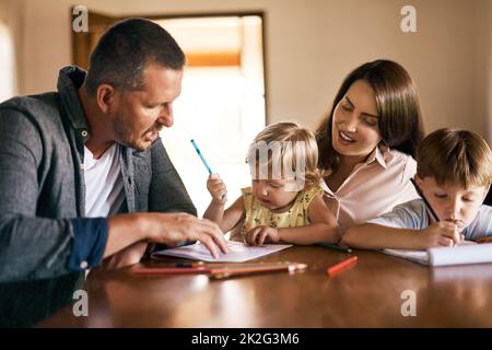 Ihre Kinder in kreatives Spielen einzubinden. Aufnahme einer jungen vierköpfigen Familie, die zu Hause kreativ zusammen zeichnet. Stockfoto