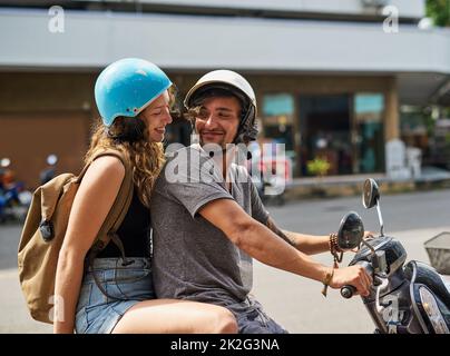 Gehen wir auf ein Abenteuer. Aufnahme von zwei glücklichen Rucksacktouristen, die ein Motorrad durch eine fremde Stadt fahren. Stockfoto