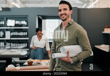 Meine Pläne sind fertig und bereit, lebendig zu werden. Aufnahme eines jungen Architekten, der in einem Büro zusammengerollte Entwürfe hält. Stockfoto