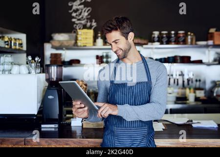 Verwaltung seiner Unternehmenswebsite. Ein kurzer Screenshot eines hübschen jungen Baristas, der ein Tablet in seinem Coffee Shop verwendet. Stockfoto