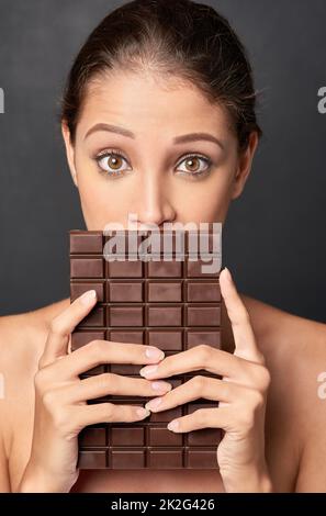 Shes ein Liebhaber von Schokolade. Studioaufnahme einer attraktiven jungen Frau, die von etwas Süßem verlockt wird. Stockfoto