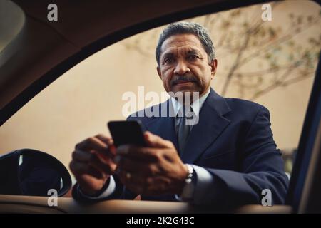 SMS schreiben und fahren ist ein ernsthaftes Geschäft. Aufnahme eines reifen Geschäftsmannes, der ein Telefon benutzt, während er sich an sein Auto lehnt. Stockfoto