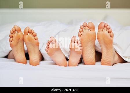 Halte deine Füße hoch. Aufnahme einer nicht erkennbaren Familie Füße nebeneinander im Bett positioniert, während sie zu Hause am Morgen schlafen. Stockfoto