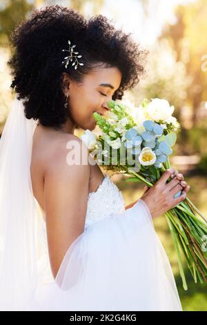 Der süße Geruch von Liebe und Glück. Aufnahme einer glücklichen und schönen jungen Braut, die an ihrem Hochzeitstag im Freien ihren Blumenstrauß riecht. Stockfoto