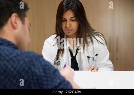 Ich brauche nur, dass Sie dieses Aufnahmeformular ausfüllen Aufnahme eines Arztes, der einem Mann beim Einfüllen von Papierkram in einem Krankenhaus hilft. Stockfoto