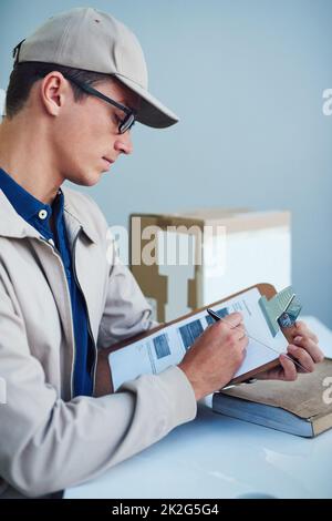 Hart arbeiten, um seine Lieferungen pünktlich zu erhalten. Aufnahme eines Kuriers, der auf einem Clipboard schreibt. Stockfoto