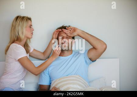 Sie weiß, wie sie sich um ihn kümmern muss. Aufnahme einer Frau, die die Temperatur ihres Mannes einnahm. Stockfoto