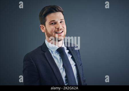 Du musst das Teil anschauen. Studioaufnahme eines fröhlichen jungen Geschäftsmannes, der vor dunklem Hintergrund steht. Stockfoto