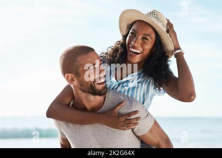 Der Sommer hält sie am Lächeln. Aufnahme eines jungen Mannes mit Huckepack seiner Freundin am Strand. Stockfoto