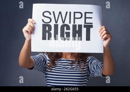 Es ist ein Match. Studio-Aufnahme einer jungen Frau mit einem Schild, auf dem ein Rechtswisch vor grauem Hintergrund gedruckt ist. Stockfoto