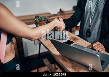 Ich hoffe, Sie genießen unsere Dienste hier. Gekürzte Aufnahme eines unbekannten Fitnesstrainers, der einem Sportmitglied an der Rezeption eines Fitnessstudios die Hand schüttelt. Stockfoto