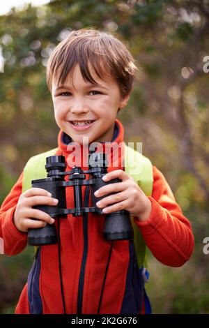 Auf der Suche nach meinem nächsten Abenteuer. Porträt eines glücklichen Jungen mit einem Fernglas im Wald. Stockfoto