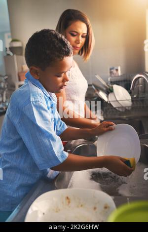 Reinigung bis das Geschirr makellos ist. Aufnahme einer Mutter und eines Sohnes, die zusammen Geschirr waschen. Stockfoto