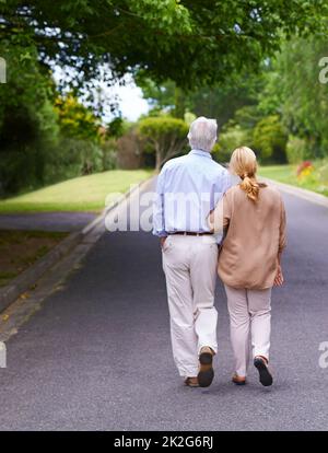 Sie haben sich in einer eigenen Welt verloren. Rückansicht eines älteren Paares, das zusammen spazieren geht. Stockfoto