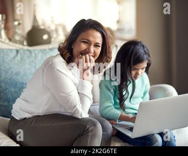 Überwachte Internetsitzungen, da die Online-Sicherheit zu Hause beginnt. Porträt einer glücklichen Frau, die neben ihrer Tochter sitzt, während sie zu Hause ein Notebook benutzt. Stockfoto