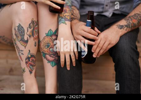 Tattoos sind eine andere Form der Körpersprache. Ein kurzer Schuss eines Paares mit Tätowierungen am Körper und Getränken in den Händen. Stockfoto