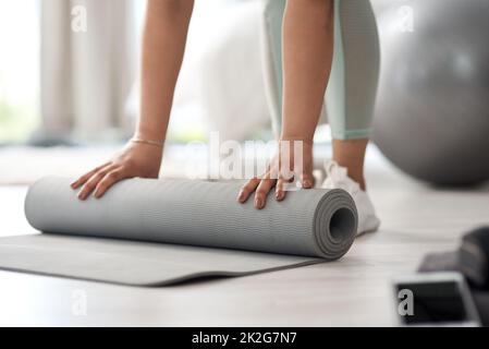 Beginnen Sie, und Sie werden die Änderung sehen. Nahaufnahme einer unkenntlichen Frau, die zu Hause eine Trainingsmatte auf den Boden rollt. Stockfoto