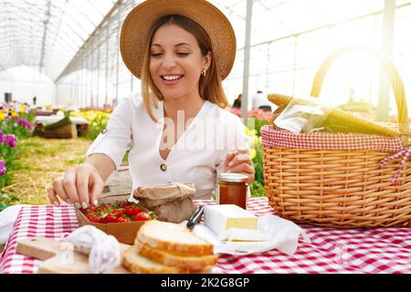 Lächelnd schönes Mädchen mit Picknick. Junge Frau nimmt eine Erdbeere. Frische Ernte und Null-Kilometer-Lebensmittel im Land im Frühling. Stockfoto