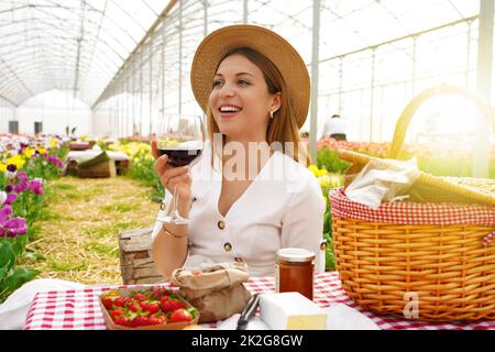 Picknick im Blumen-Gewächshaus mit Null-Kilometer-Produkten. Fröhliche Frau, die ein Weinglas auf der Seite in Bauernhaus der Toskana, Italien. Stockfoto