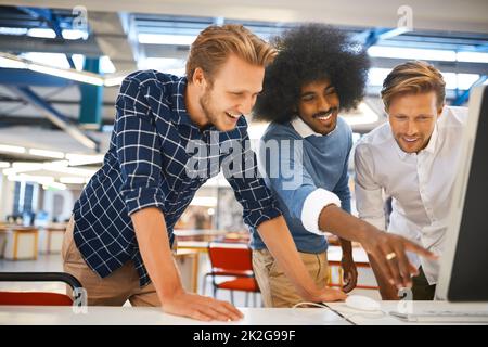 Dreies Unternehmen. Eine kurze Aufnahme von drei jungen männlichen Designern, die in ihrem Büro an einem Schreibtisch arbeiten. Stockfoto