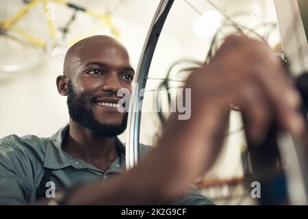 Dieses Bike ist bereit für das Wochenende. Aufnahme eines hübschen jungen Mannes, der allein in seinem Geschäft steht und ein Fahrradrad repariert. Stockfoto