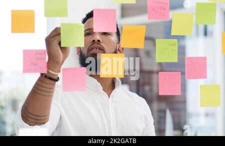 Was hält Sie davon ab, größer zu denken. Aufnahme eines jungen Geschäftsmannes beim Brainstorming mit Haftnotizen an einer Glaswand in einem Büro. Stockfoto