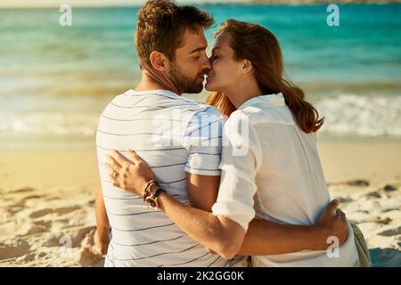 Sommerromantik kann nicht besser sein als dieses. Aufnahme eines jungen Paares, das sich an einem Sommertag am Strand küsst. Stockfoto