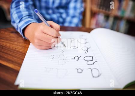 Seine Handschrift üben. Aufnahme eines unerkennbaren jungen Jungen, der in der Schule in einem Buch schreibt. Stockfoto