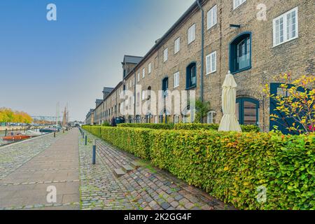 Viele dreistöckige Gebäude aus grauen Ziegeln auf einer Straße mit Steinpflaster in der Nähe des Flusskanals in der Nachbarschaft Christianshavn. Kopenhagen, Dänemark Stockfoto