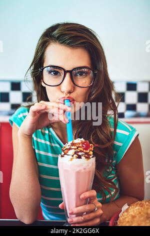 Schütteln Sie es auf. Das verkürzte Porträt einer attraktiven jungen Frau, die in einem Retro-Diner einen Milchshake genießt. Stockfoto