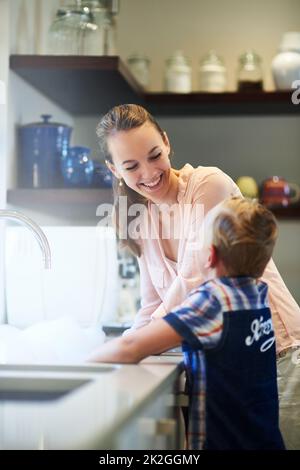 Kleben zu Hause. Aufnahme einer Mutter und eines Sohnes, die zusammen Geschirr waschen. Stockfoto