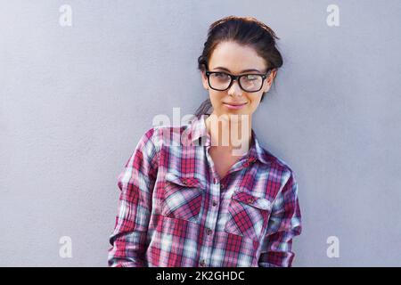 Sie trägt ihren eigenen Stil mit Stolz. Porträt einer attraktiven jungen Frau mit Brille und kariertem Hemd. Stockfoto