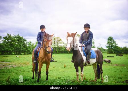 Sattel hoch, es ist an der Zeit zu fahren. Aufnahme von zwei Mädchen im Teenageralter, die auf einer Ranch reiten. Stockfoto