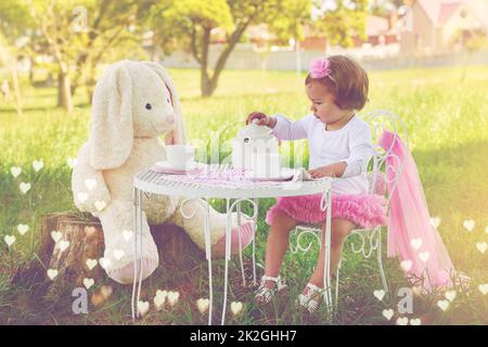 Noch etwas Tee, Mrs. Rabbit. Aufnahme eines niedlichen kleinen Mädchens, das draußen auf dem Rasen eine Teeparty mit ihrem Stofftier hat. Stockfoto