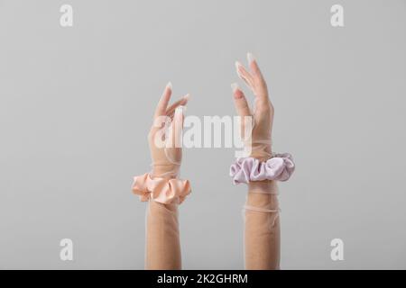 Weibliche Hände in Handschuhen mit Seidenschrunchies auf hellem Hintergrund Stockfoto