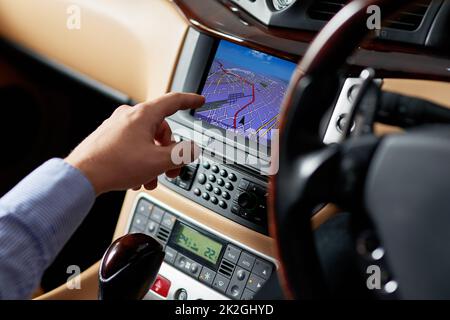 Lassen Sie die Technologie den Weg vorgeben. Nahaufnahme eines Fahrers, der ein GPS-Gerät eines Autos verwendet, um eine Wegbeschreibung zu finden. Stockfoto