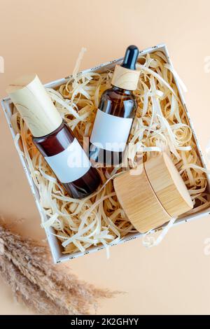 Beauty-Abonnement Box Vorbereitung im Öko-Stil. Geschenkbox mit natürlichen Hautpflegeprodukten - Gesichtscreme, Essenz und Serum in dunklen Glasflaschen mit b Stockfoto