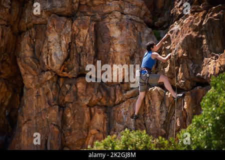 Fest anhängen. Eine breite Aufnahme einer jungen Frau beim Klettern. Stockfoto