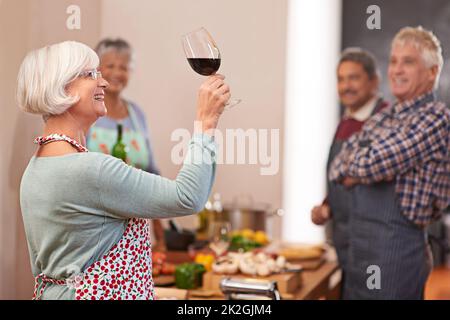 Sie serviert immer die besten Jahrgänge. Aufnahme einer älteren Frau, die ihren Wein mit Freunden im Hintergrund ansieht. Stockfoto