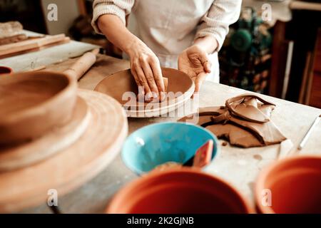 Der Schwamm saugt überschüssiges Wasser auf. Ausgeschnittene Aufnahme eines nicht erkennbaren Handwerkers, der in einer Töpferwerkstatt arbeitet. Stockfoto