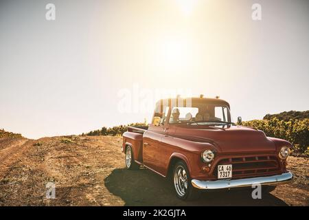 Mit dem alten LKW für eine Kreuzfahrt. Aufnahme einer fröhlichen jungen Familie, die in einem roten Pickup-Truck auf einer Landstraße vor der Tür fährt. Stockfoto