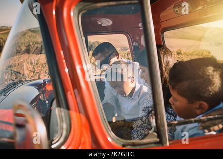 Nur ein kurzer Pitstop, bevor es weiter geht. Aufnahme einer fröhlichen jungen Familie, die in einem roten Pickup-Truck auf einer Landstraße vor der Tür fährt. Stockfoto