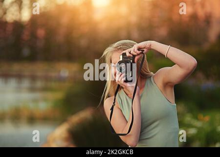 Lassen Sie keinen Moment unbefangen. Porträt einer jungen Frau, die draußen mit ihrer Kamera fotografiert. Stockfoto