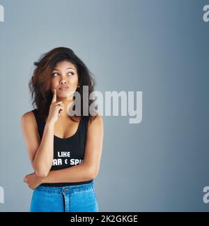 Penny für deine Gedanken. Aufnahme einer attraktiven jungen Frau, die vor grauem Hintergrund posiert. Stockfoto