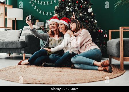 Das hier geht ins Album. Aufnahme von drei attraktiven Frauen mittleren Alters, die Selbstporträts zusammen mit einem Handy zu Hause zu Weihnachten machen. Stockfoto